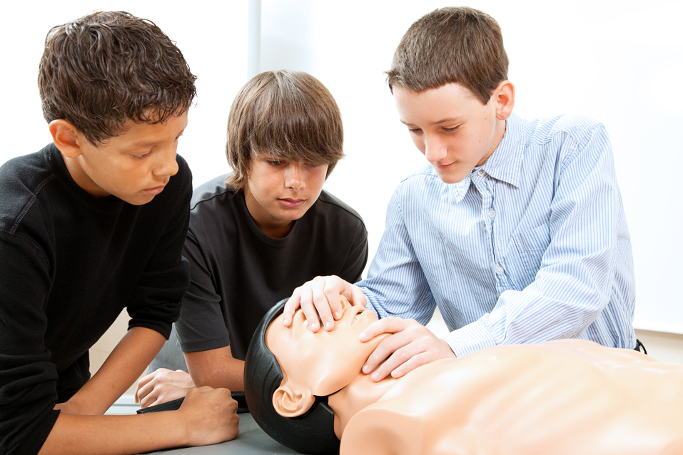 Teenage boys learn CPR life saving techniques on a mannequin.