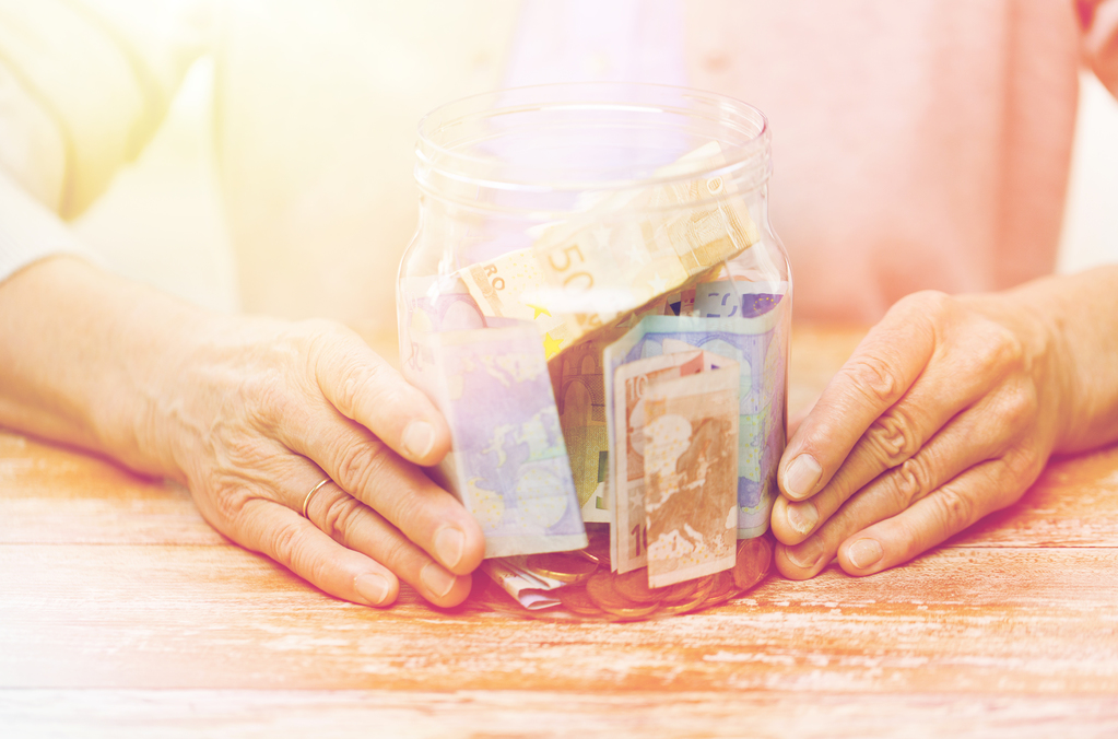 savings, money, annuity insurance, retirement and people concept - close up of senior woman hands with money in glass jar