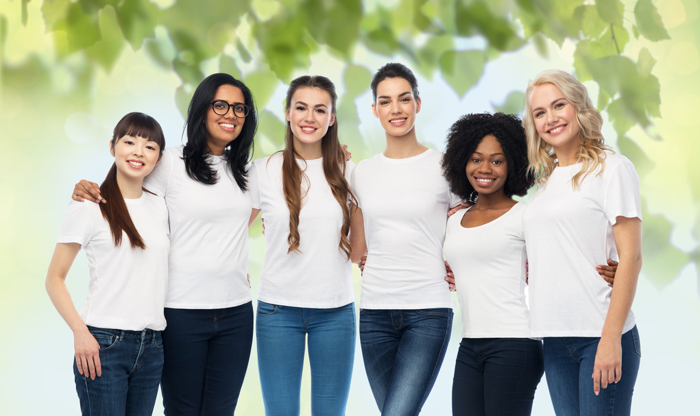 diversity, ecology and people concept - international group of happy smiling volunteer women in white blank t-shirts hugging over green natural background