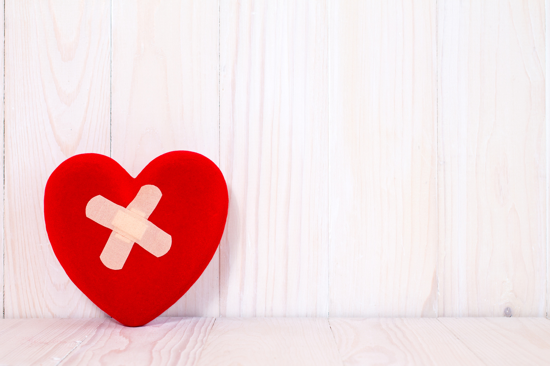 Injured heart with plaster on the wooden background