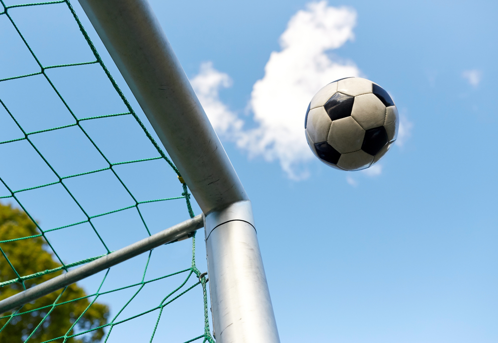 sport, soccer and game - ball flying into football goal net over blue sky