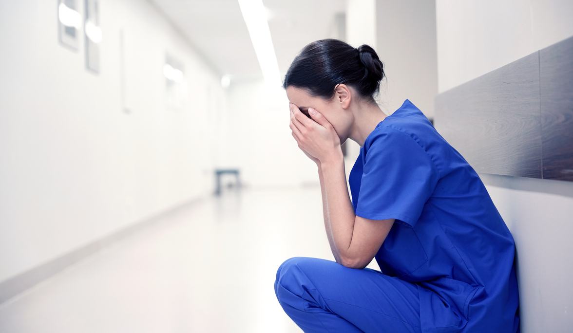 people, medicine, healthcare and sorrow concept - sad or crying female nurse at hospital corridor