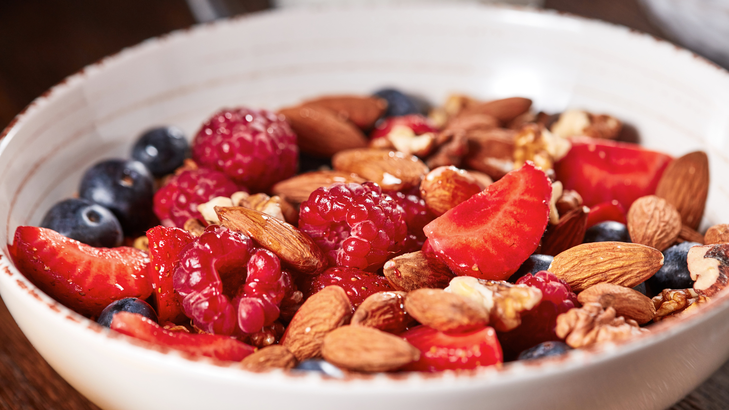 Dietary natural breakfast with fresh organic ingredients - berries, granola, nuts in a white bowl on a wooden table. Healthy vegetarian eating.